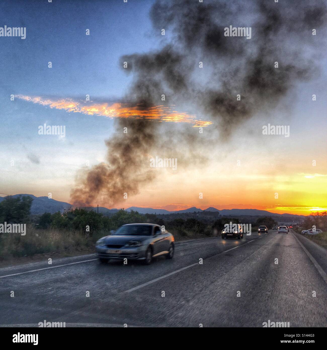 Smoke drifting across road and traffic at sunset, with police car in the distance - Smartphone Captured Stock Image