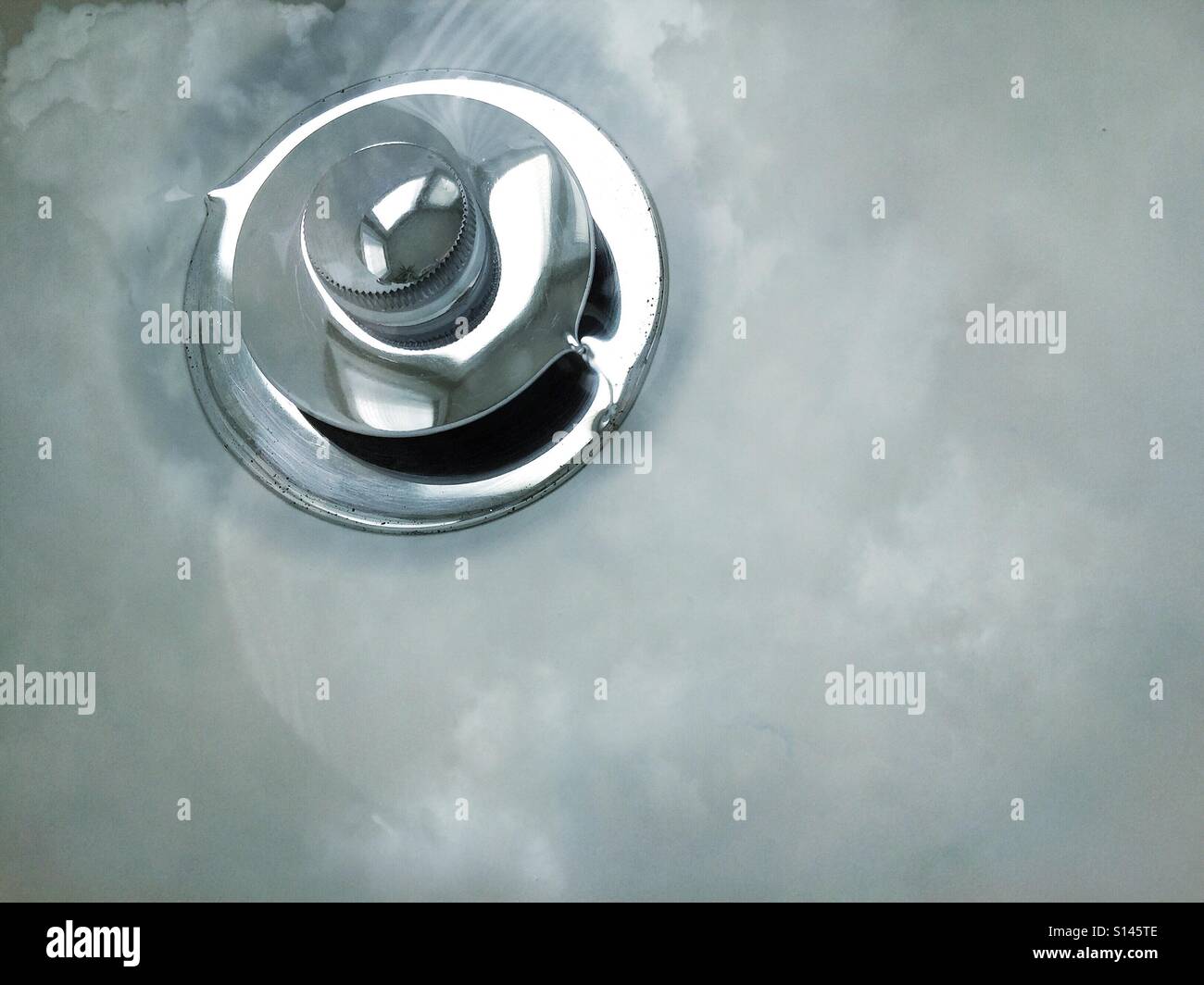 Clouds appear to be reflected in the last of the water as it swirls down the drain. - Smartphone Captured Stock Image