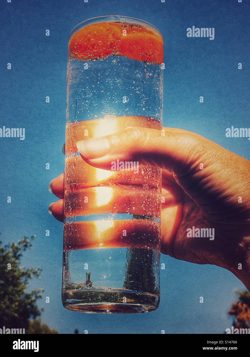 Looking up to Woman holding a drink in a tall glass with limes at the top - Smartphone Captured Stock Image