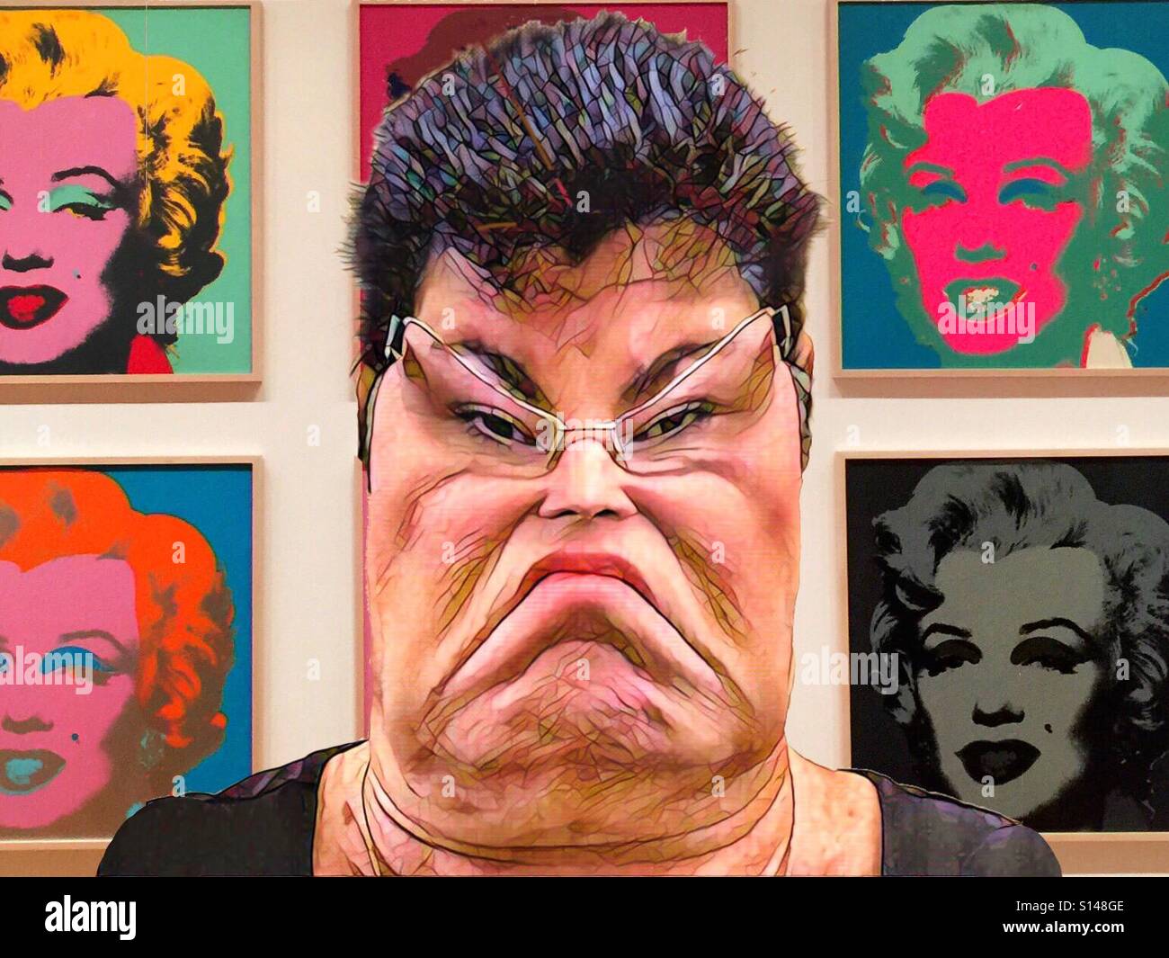 An abstract artwork featuring the square, distorted face of a dark haired Caucasian woman wearing glasses in front of an Andy Warhol series of pop art paintings of Marilyn Monroe Stock Photo