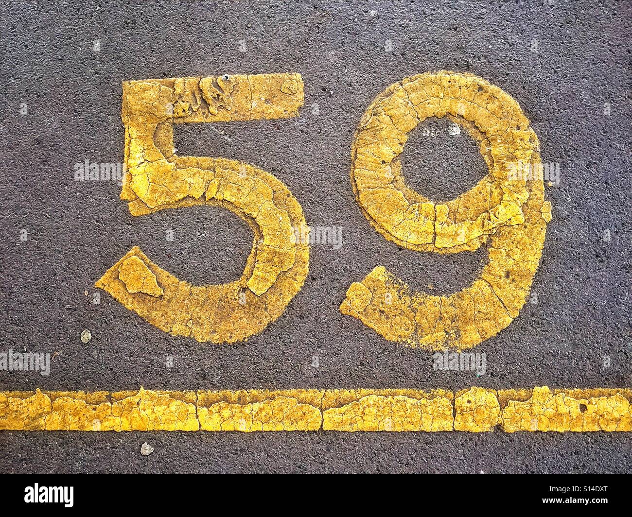 The number Fifty Nine (59) is stencilled in yellow paint onto a piece of tarmac to help identify a car parking space. Photo Credit © COLIN HOSKINS. - Smartphone Captured Stock Image