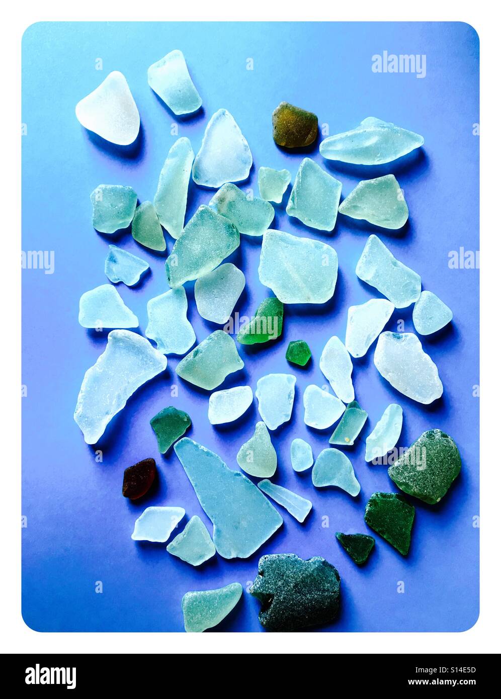 Sea glass collection of various blue, green and white glass pieces on blue background - Smartphone Captured Stock Image