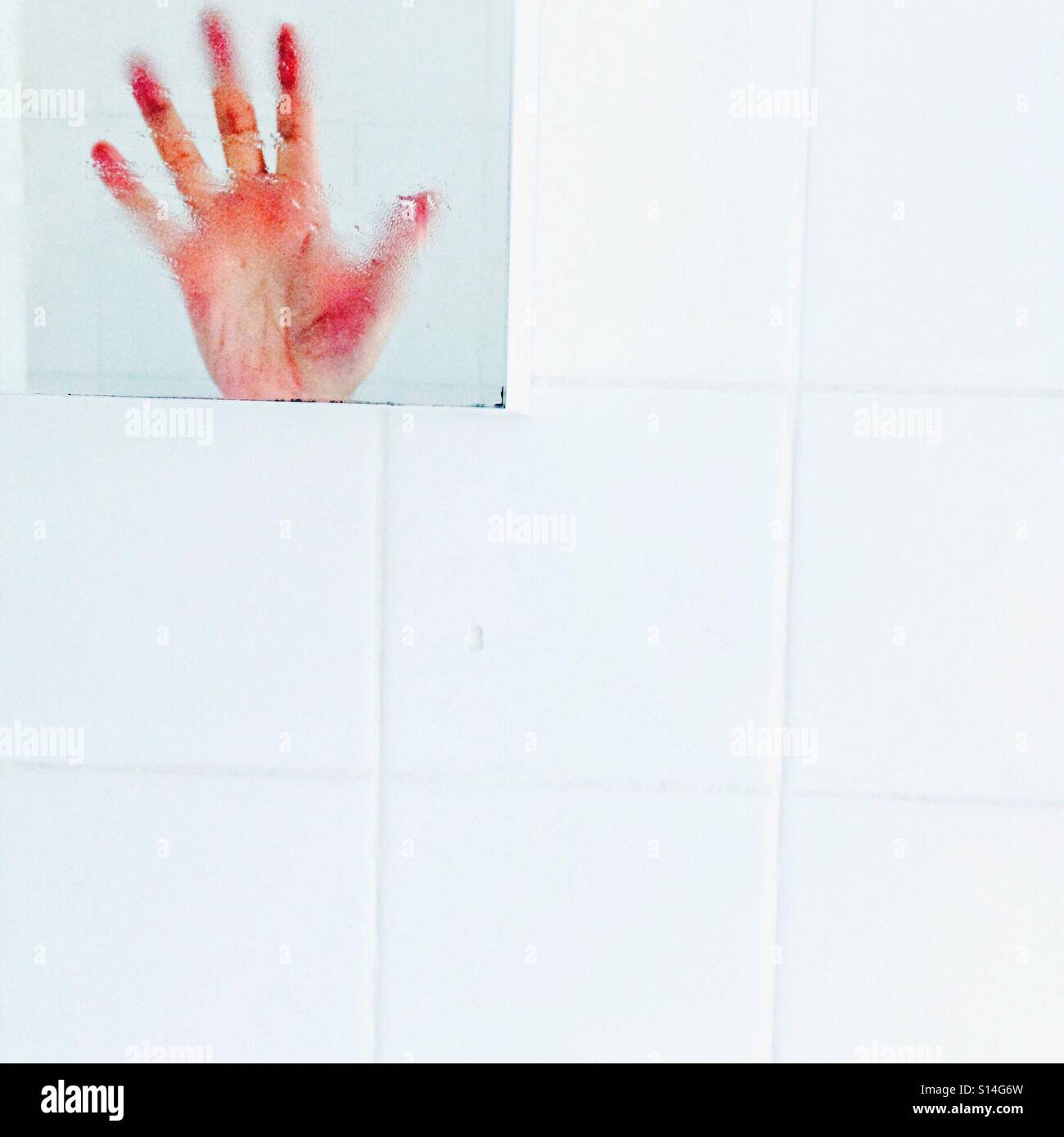 Hands Up !  A hand reflected in a bathroom mirror on white tiles Stock Photo