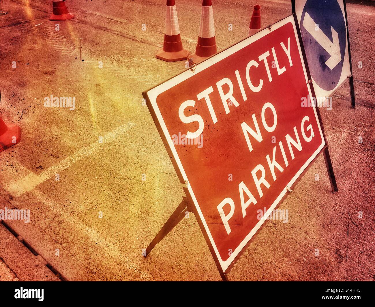 A temporary road sign announcing "STRICTLY NO PARKING" and a white arrow on a blue circular background showing motorists the direction steer. More Roadworks! Photo Credit - © COLIN HOSKINS. - Smartphone Captured Stock Image