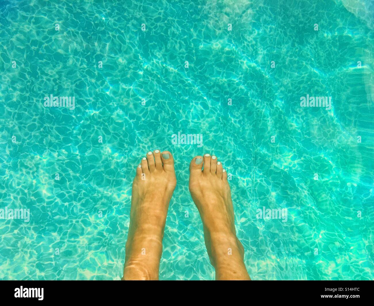 Woman's feet dangling in blue water of swimming pool on a sunny day. - Smartphone Captured Stock Image