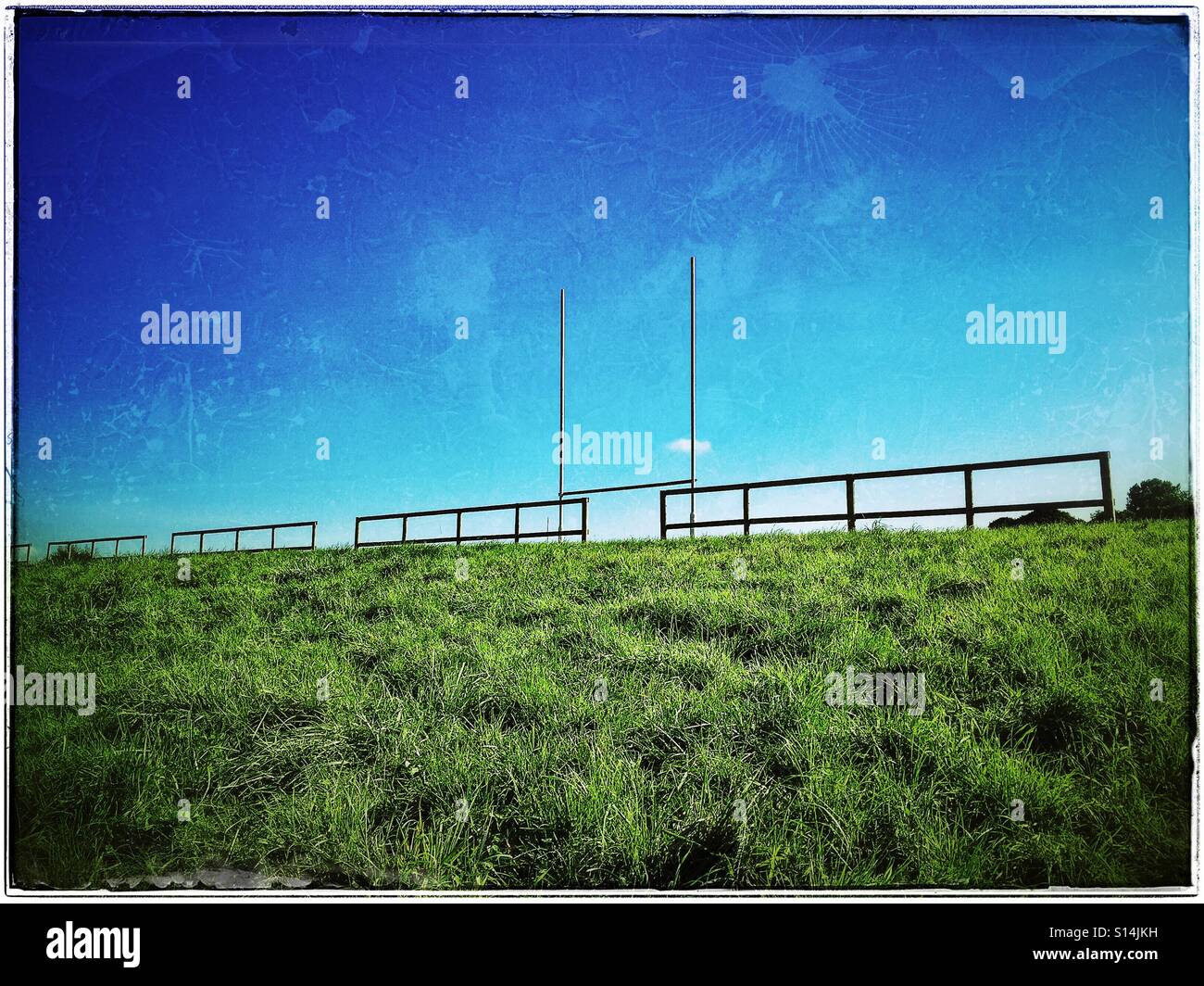 A sunshine landscape picture looking up at a Rugby Field. The area next to the Rugby pitch is uneven and the grass on the side bank is long and uneven. Photo Credit - © COLIN HOSKINS. - Smartphone Captured Stock Image
