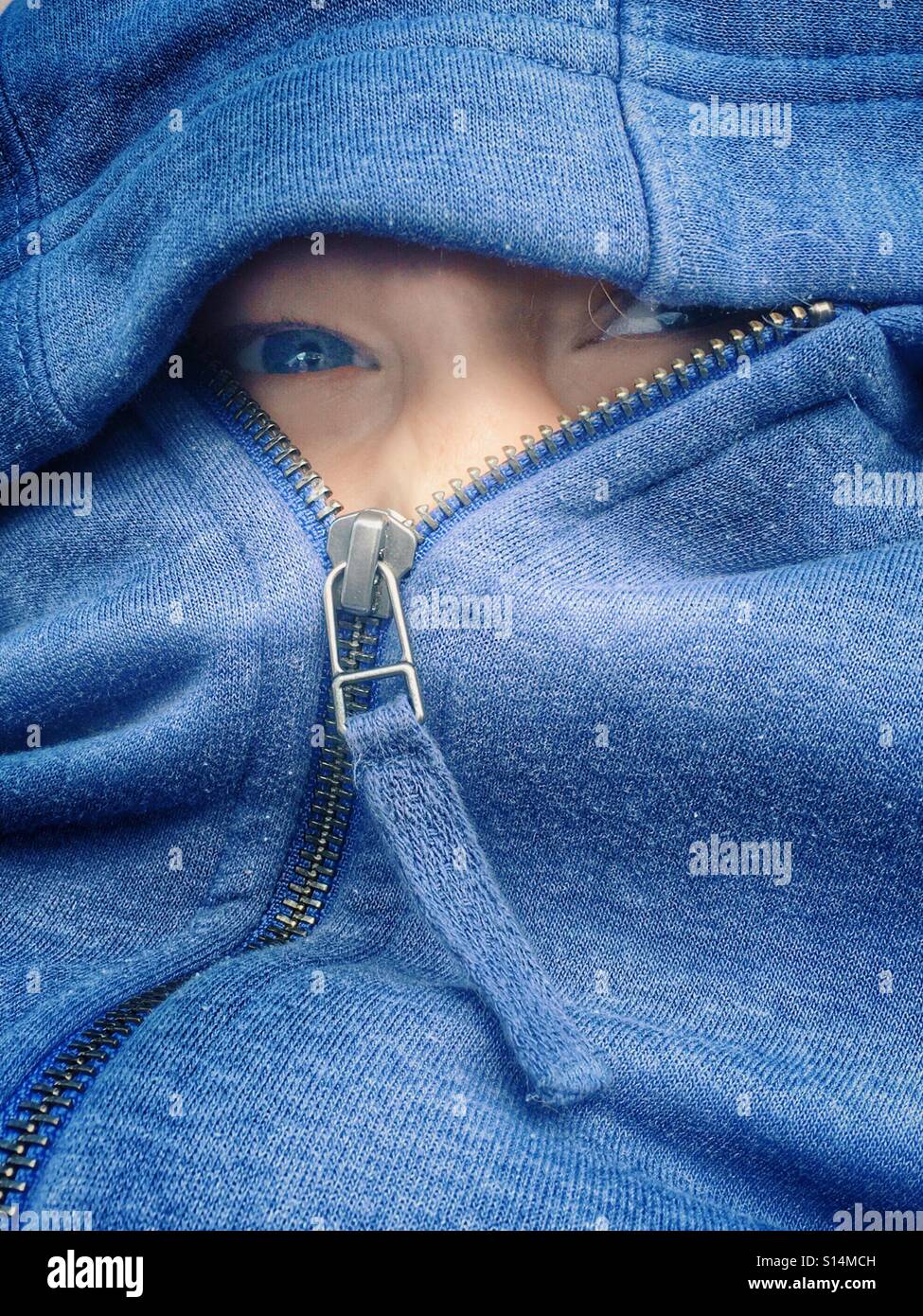 Young girl with blue eyes peering out from zipped up hoody Stock Photo