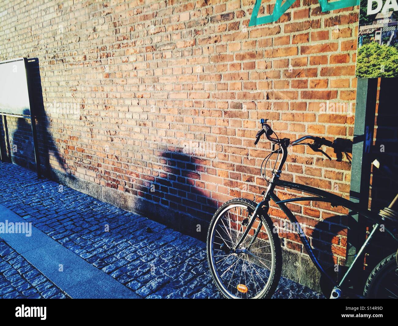 Bicycle against a brick wall and shadows at sunset in the streets of Copenhagen, Denmark, Europe - Smartphone Captured Stock Image