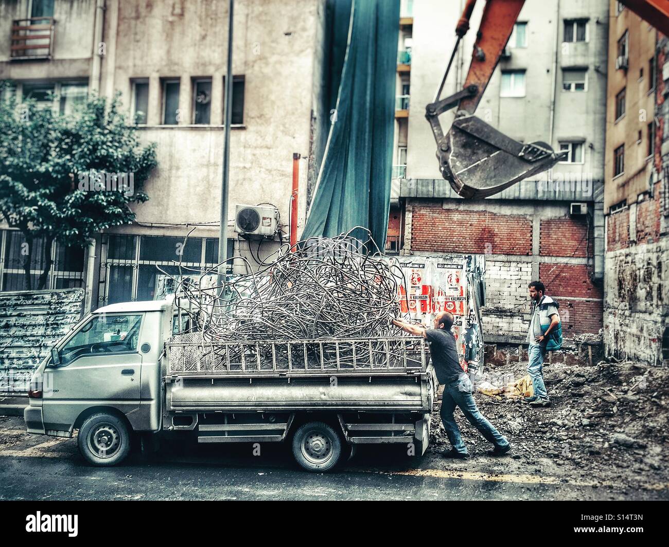 Man loading a tangle of scrap metal onto the back of a truck in an Istanbul backstreet, while his work mate looks on. - Smartphone Captured Stock Image