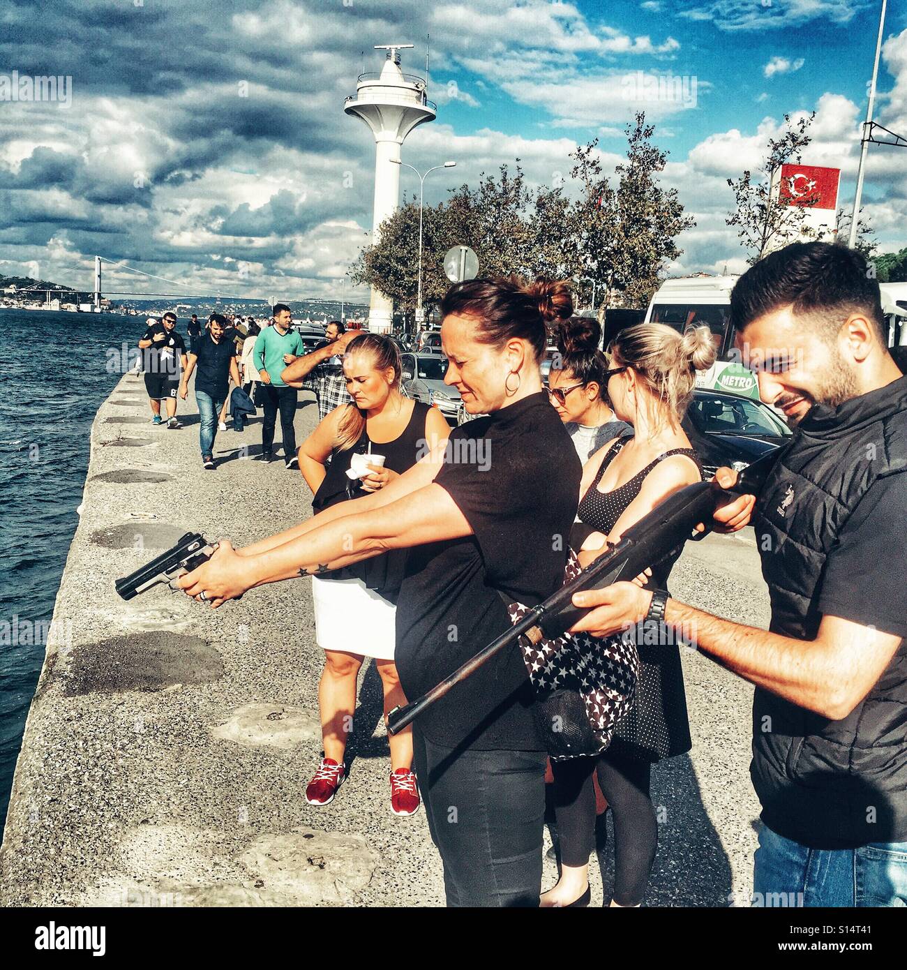 Man and woman firing guns at balloons floating in the Bosphorus, Istanbul - Smartphone Captured Stock Image