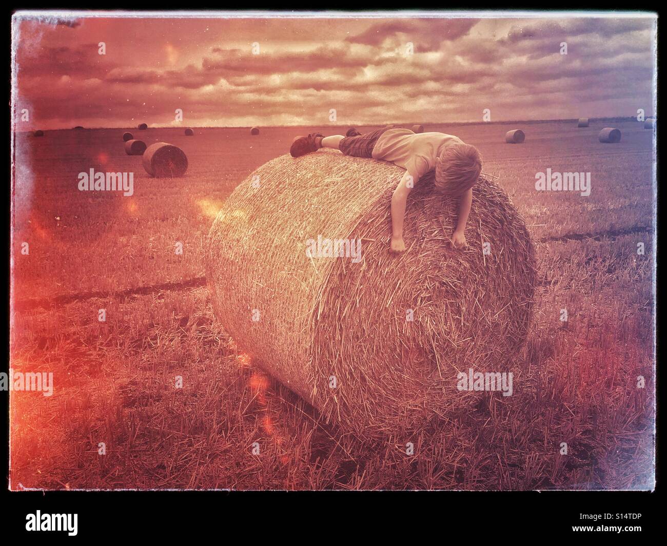 A retro film effect image of a 6 year old boy lying on top of a hay bale. Is he asleep? Has he run away from home? Is he playing truant? Is he enjoying a countryside walk with his parents?  Photo © CH - Smartphone Captured Stock Image