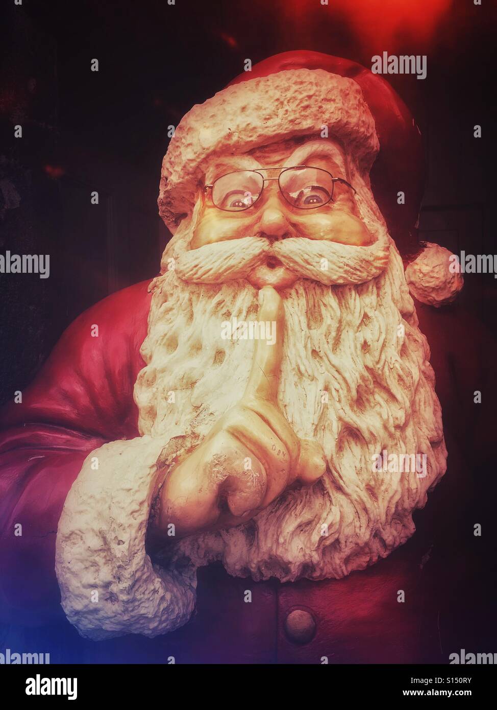 An analogue film effect image depicting a large model sculpture of Father Christmas (Santa Claus). He has his finger up to his mouth doing the 'keep quite' gesture. Photo Credit - © COLIN HOSKINS. - Smartphone Captured Stock Image