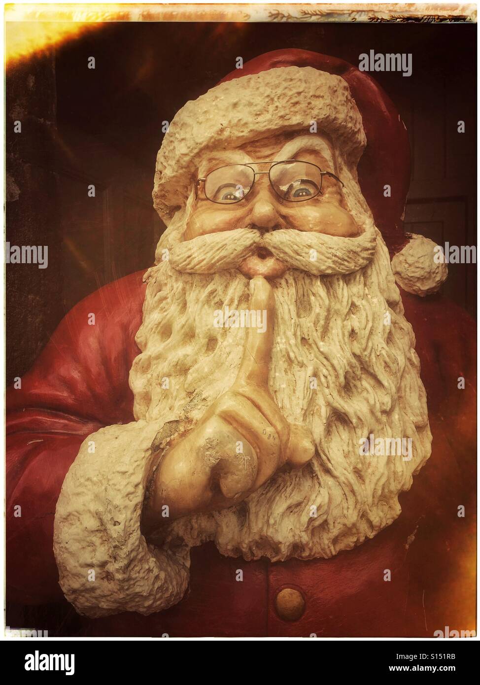 An old film effect image of a model of Father Christmas (Santa Claus). He has a large white beard, and is holding his finger up to his mouth in a gesture asking for stillness and less noise. © CH. - Smartphone Captured Stock Image