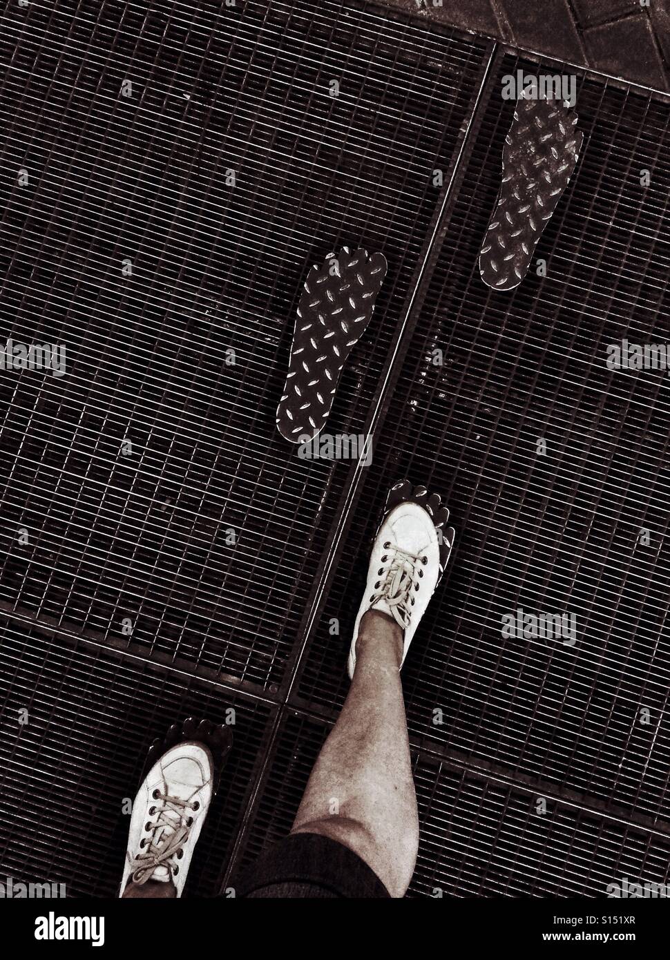 Legs walking on a metal plaque shaped like foot prints - Smartphone Captured Stock Image