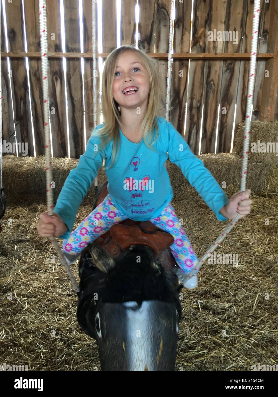 A girl swinging on a horse swing inside a barn. Stock Photo