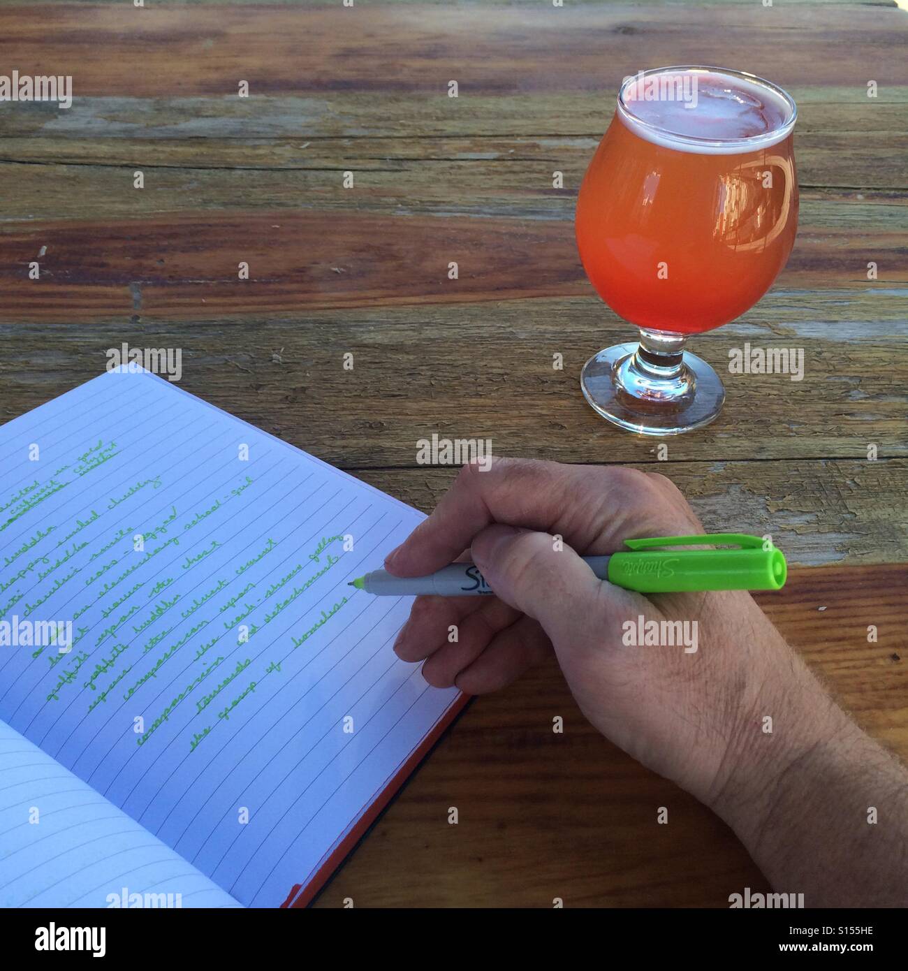 Person writing with a beer at his side. Stock Photo