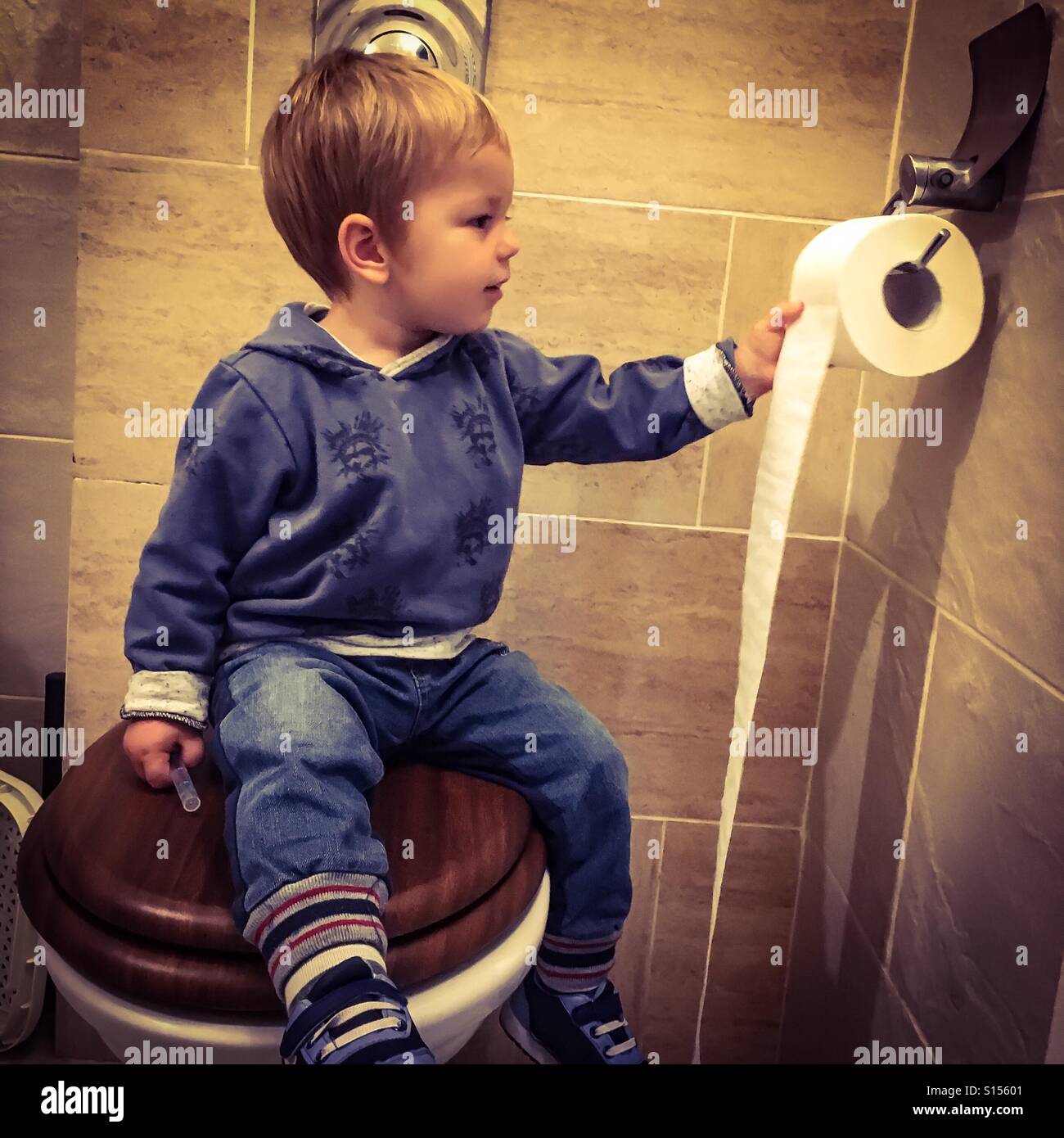 Toddler sitting on a toilet seat , having fun unrolling toilet paper Stock Photo