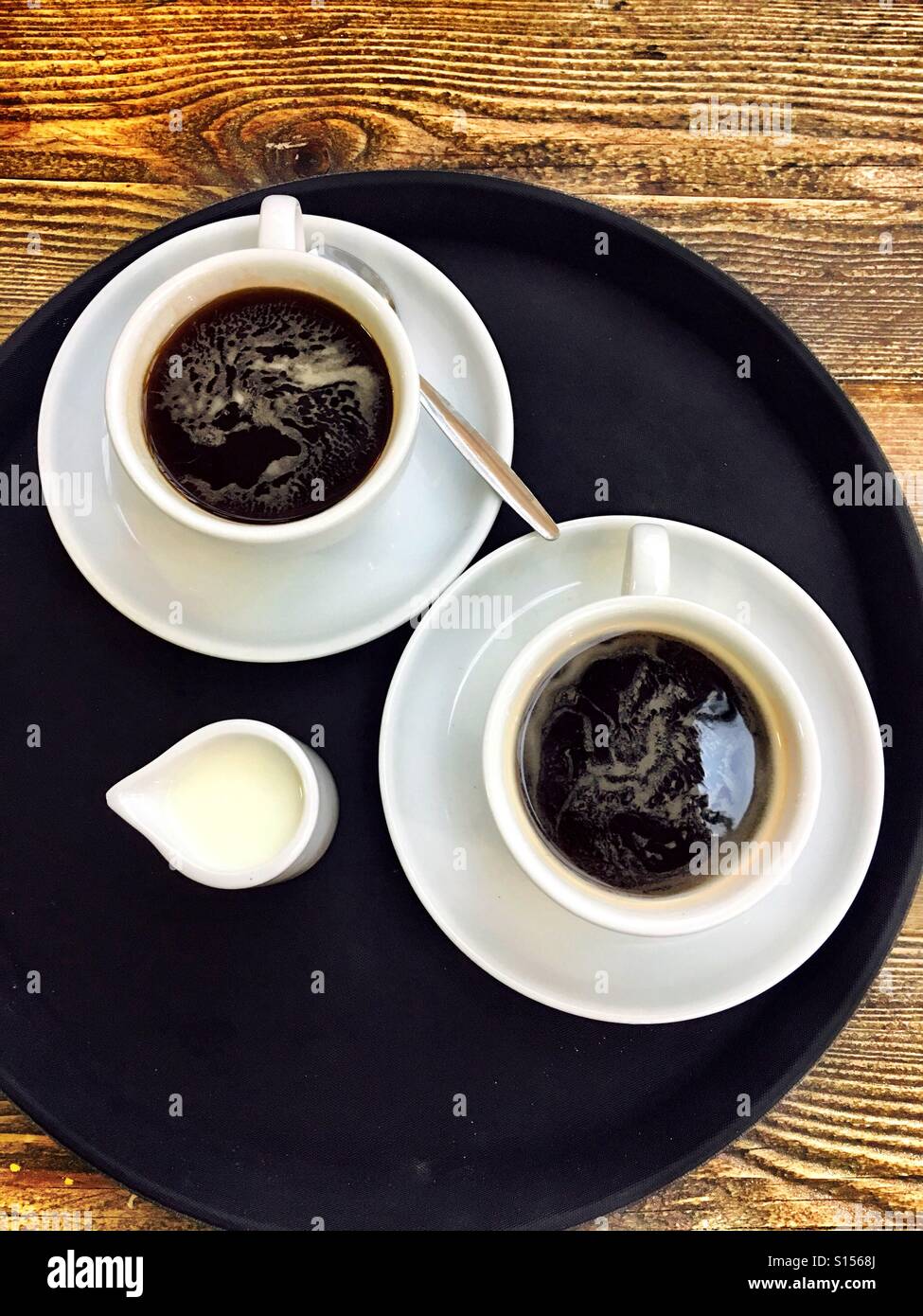 Coffee for two - Americano. Top down shot of 2 black coffees on a round, black tray, with a small jug of cold milk Stock Photo