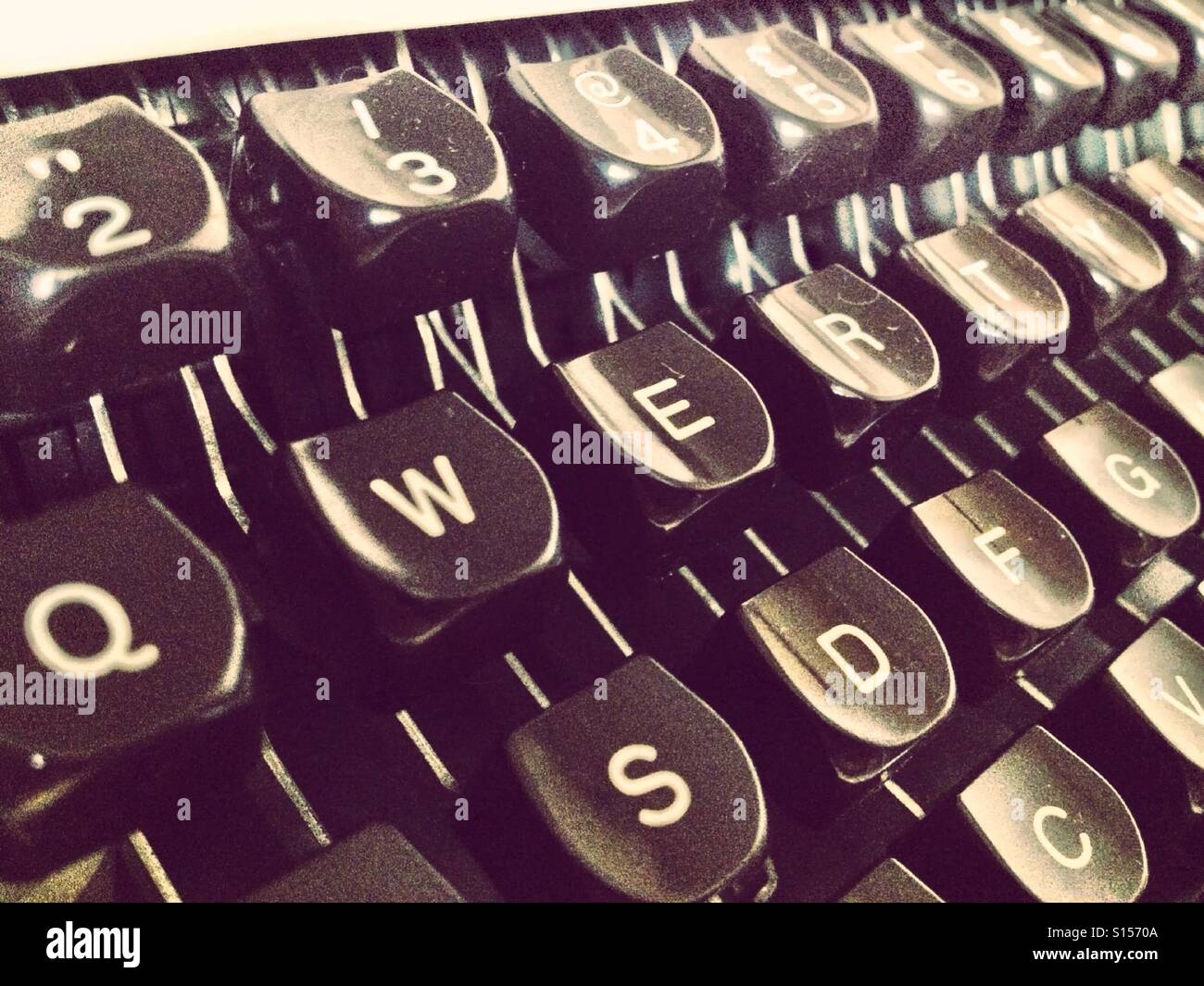 Small typewriter with keyboard in focus over a page of a book. Decoration  item. Concepts of reading, writing, old times, past. Close up. Blurred  background. Stock Photo