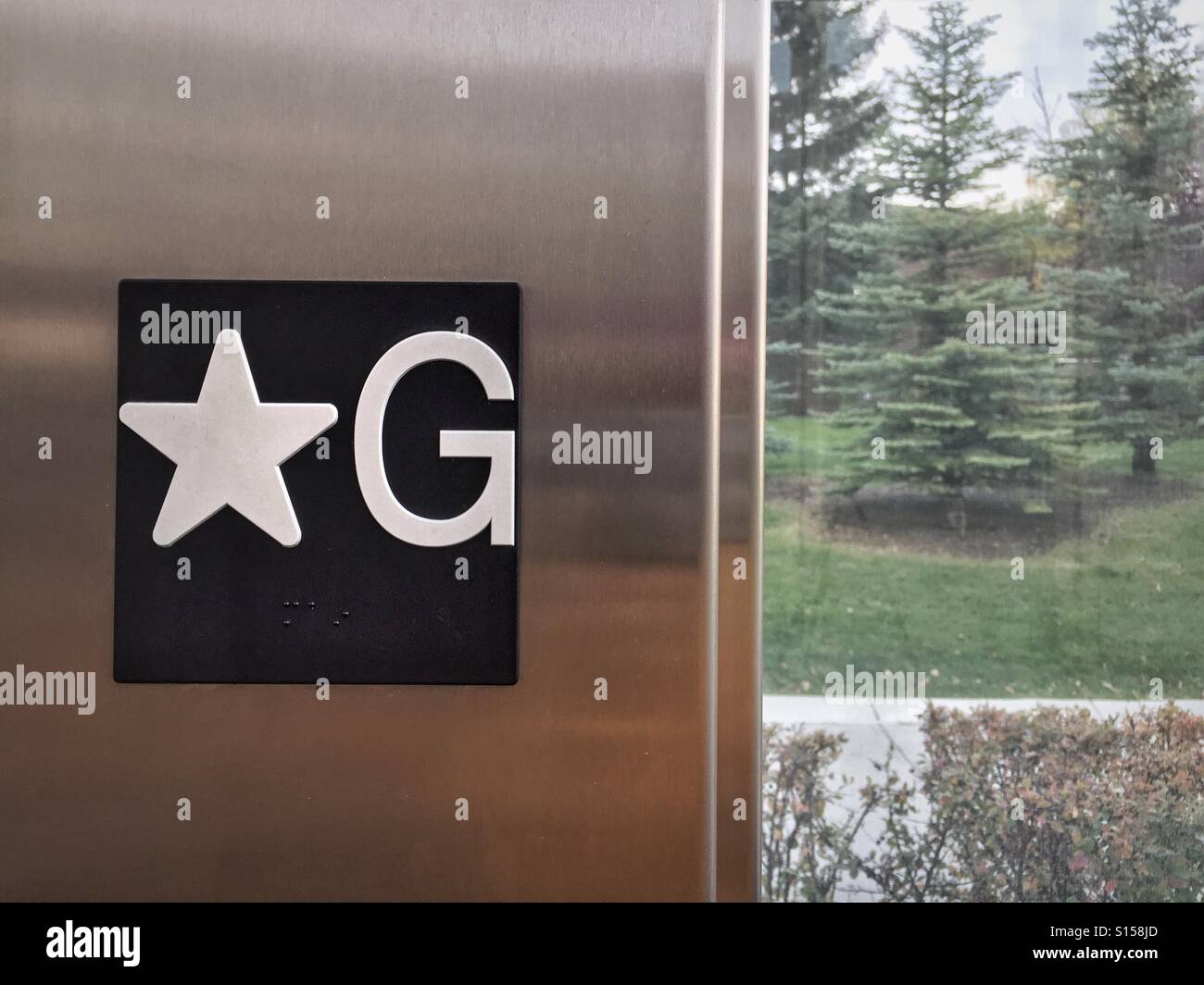 An elevator on the ground floor opens to a glass lobby and the gardens beyond. Stock Photo