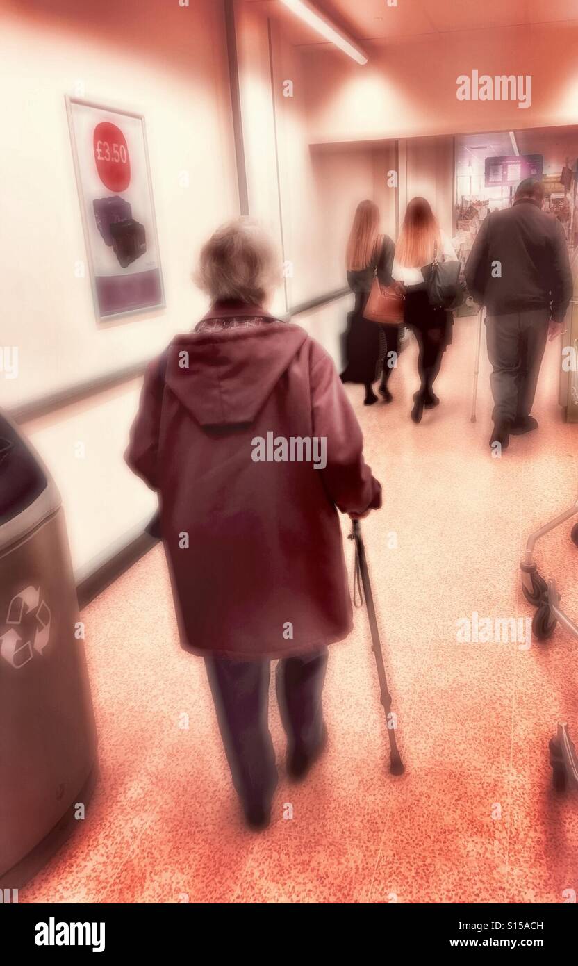 Young and old people - back view of figures walking inside a shop, nearest figure using a walking aid. Stock Photo