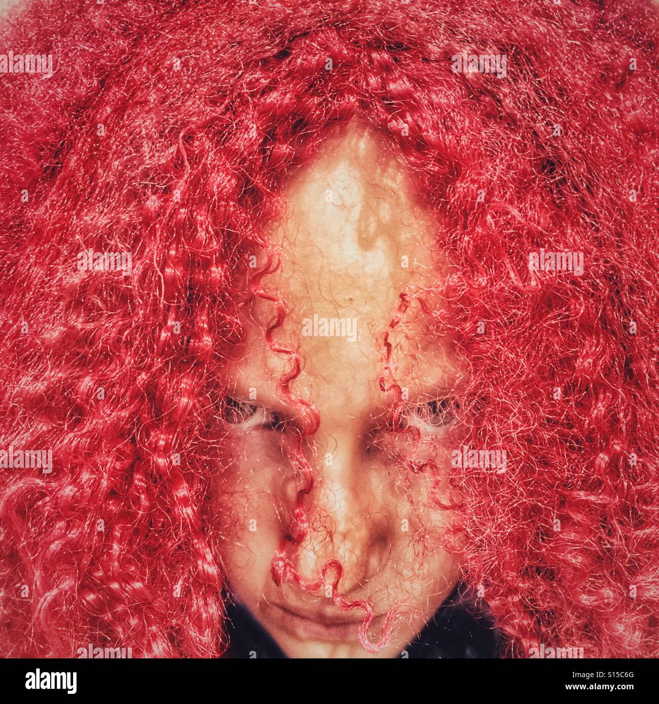 Girl peering out from behind red crimped Halloween wig Stock Photo