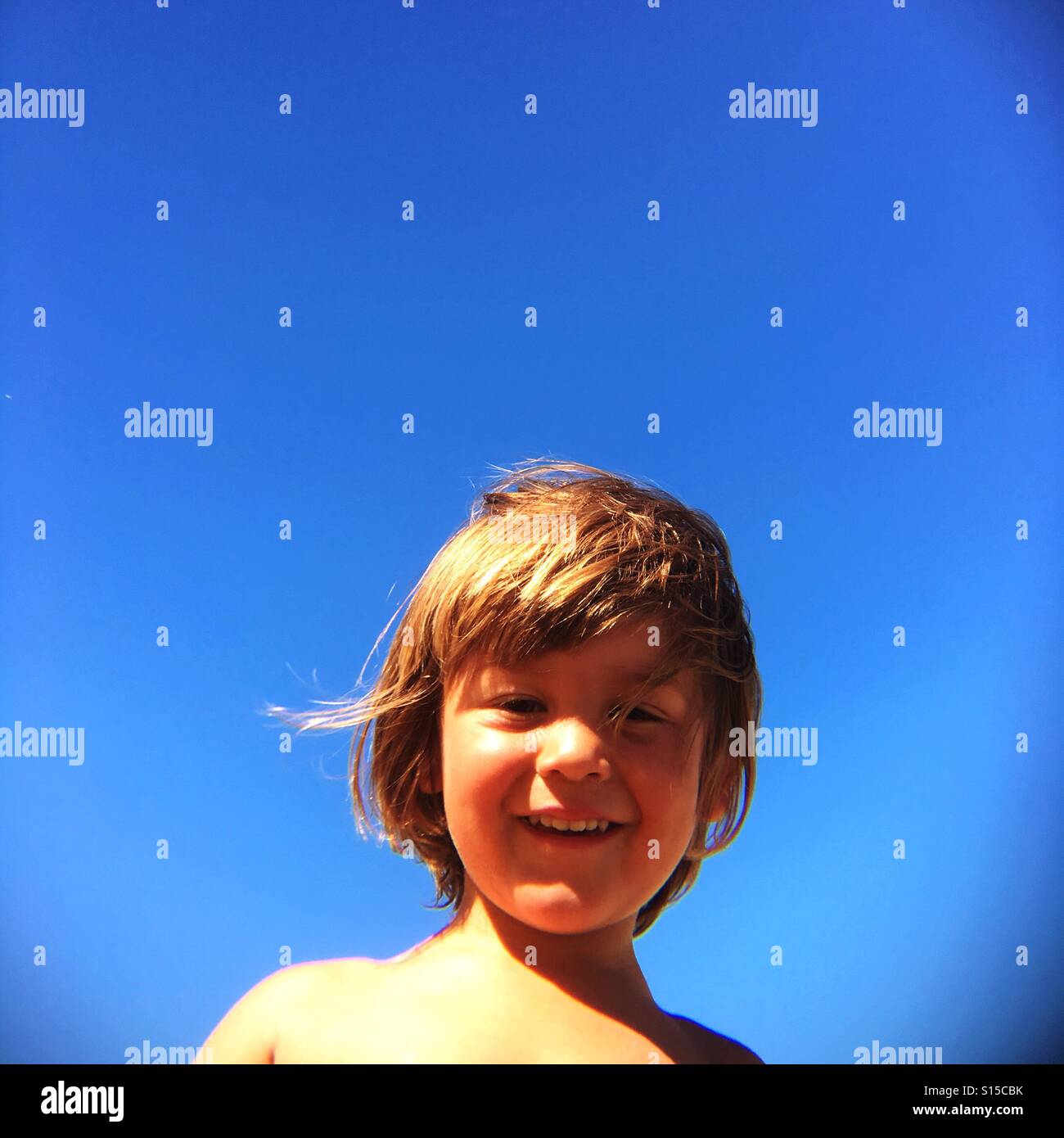 2 year old boy smiling in the sunshine with blue sky background Stock Photo