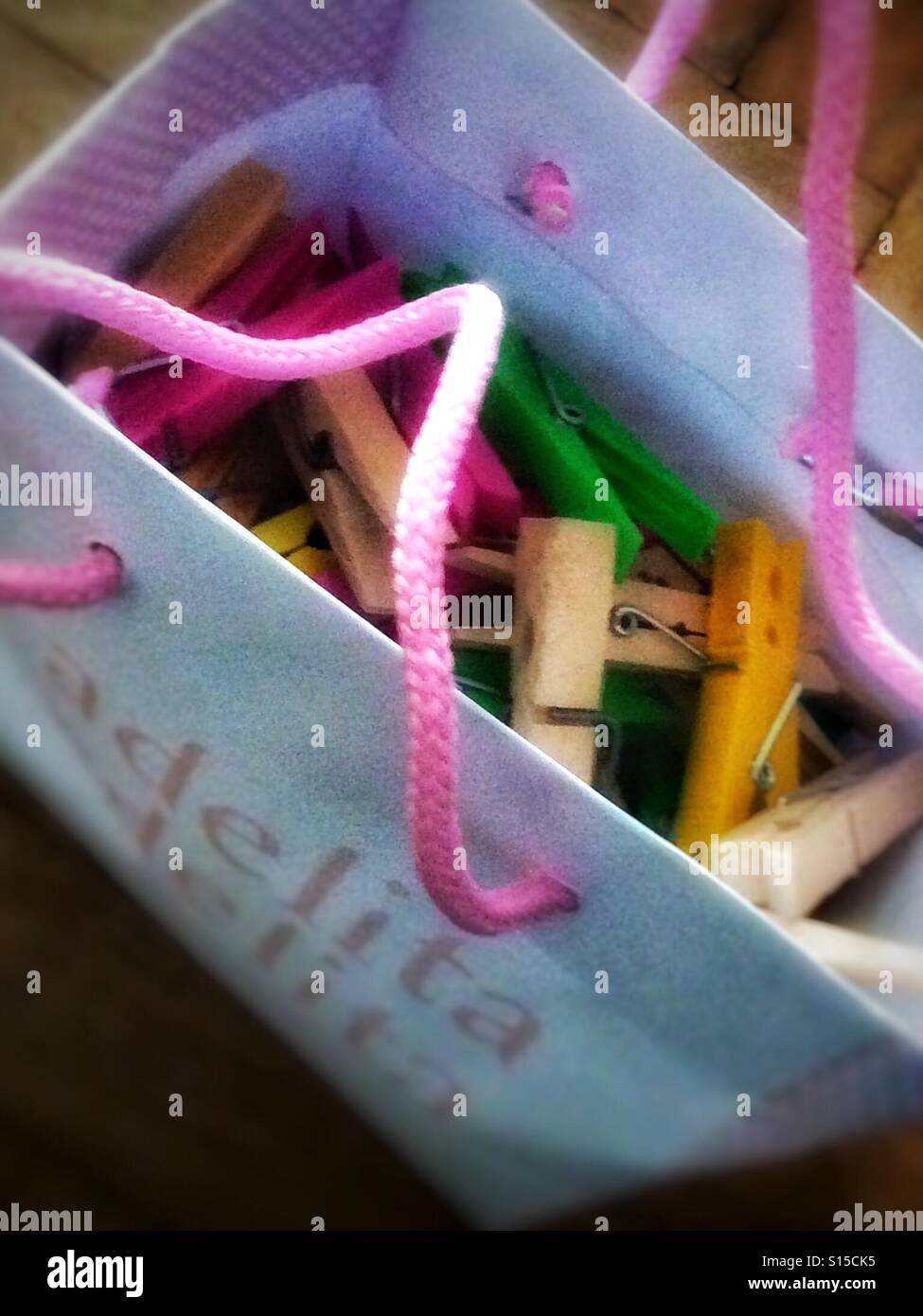 Colourful clothepegs in a small carrier bag with pink corded handles Stock Photo