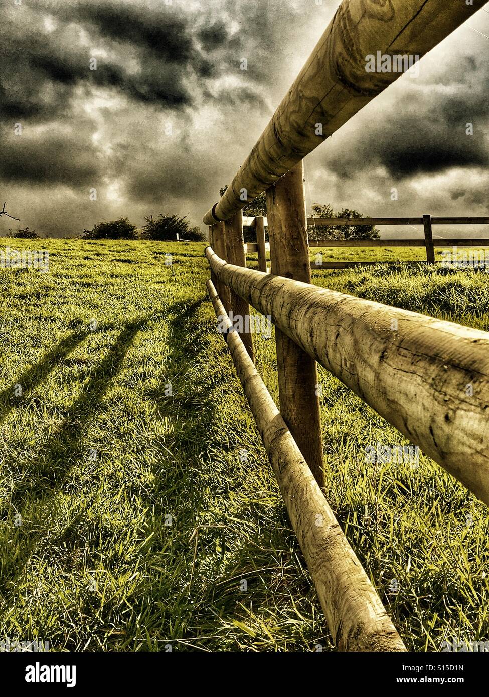 Post and rail field fence with heavy afternoon shadows and threatening sky Stock Photo