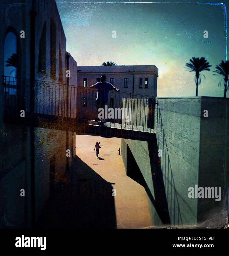Man standing on a bridge with a woman walking underneath with two palms in the distance - Smartphone Captured Stock Image