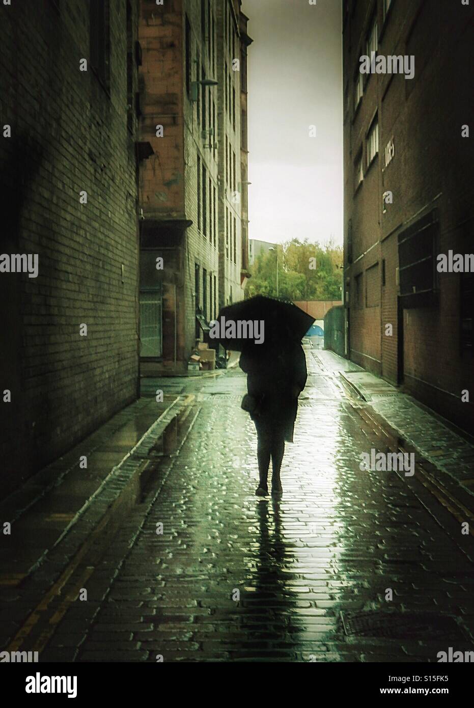 Woman with an umbrella walking along a cobbled lane when it was raining, Glasgow, Scotland, UK - Smartphone Captured Stock Image