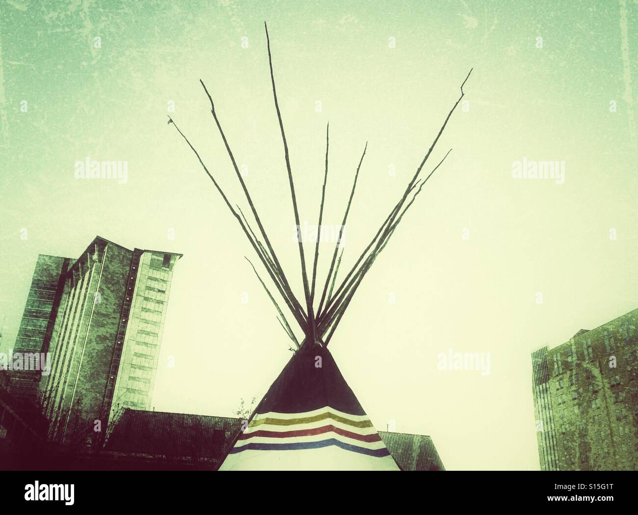 A traditional First Nations teepee stands among modern skyscrapers. Stock Photo