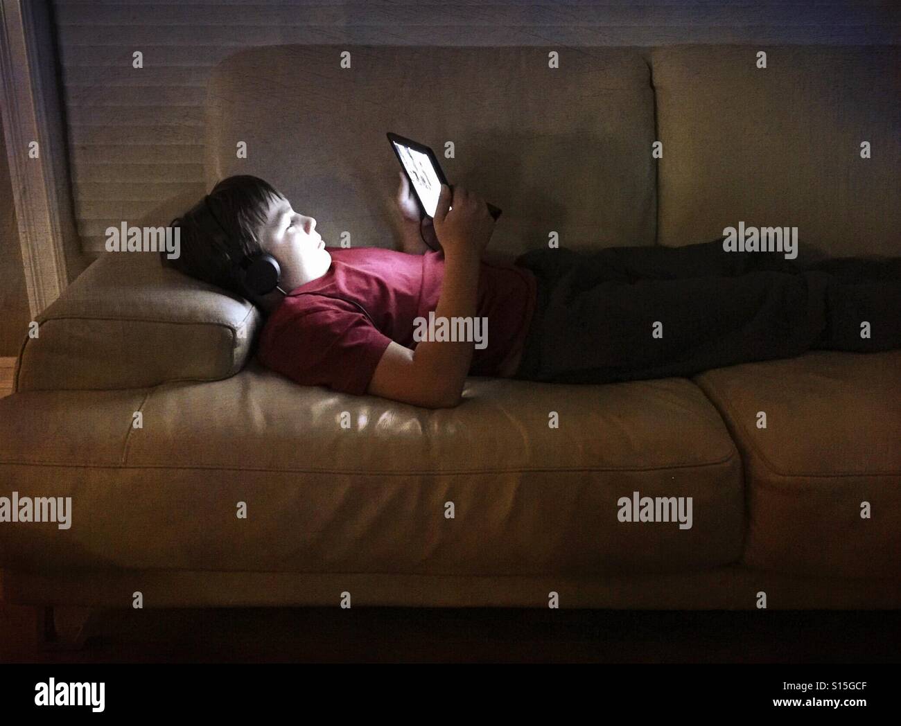 A boy plays on his tablet while lying on a couch. - Smartphone Captured Stock Image