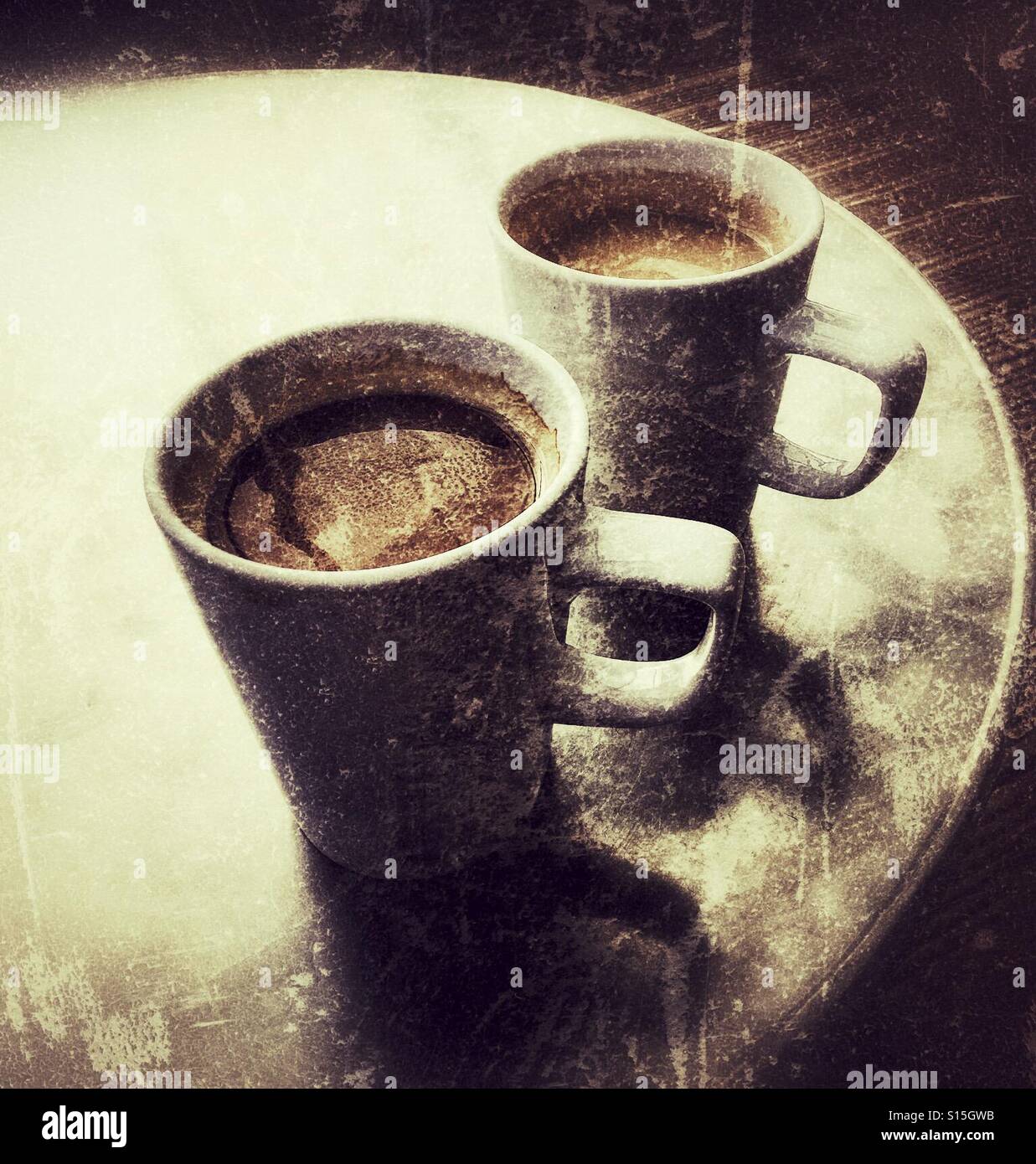 Two large coffees in white mugs on a round table with grunge overlay. Stock Photo