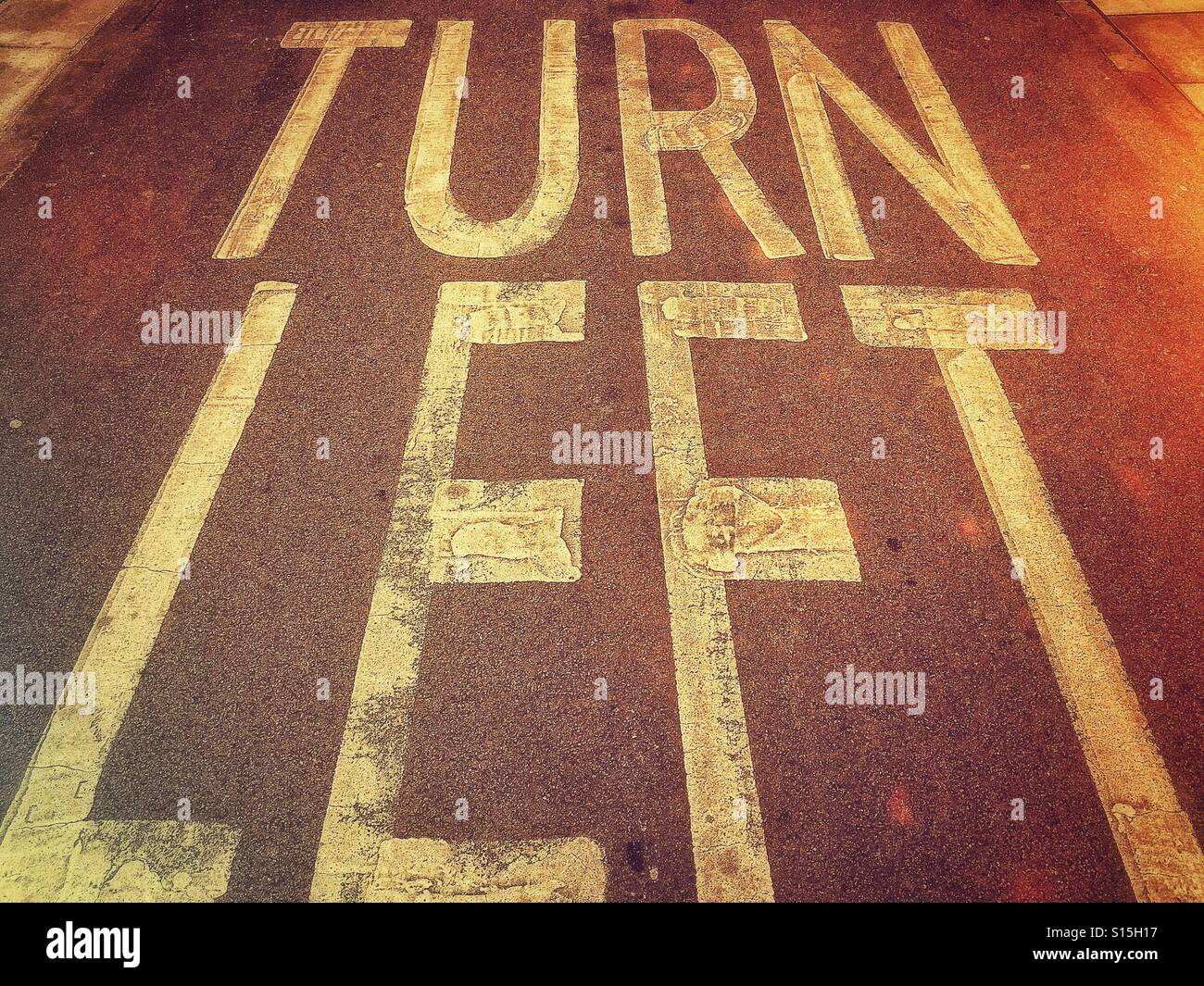 'TURN LEFT'  A retro film effect image of writing on a Tarmac road. The instructions are for road users to Turn Left up ahead. Photo Credit - © COLIN HOSKINS. - Smartphone Captured Stock Image
