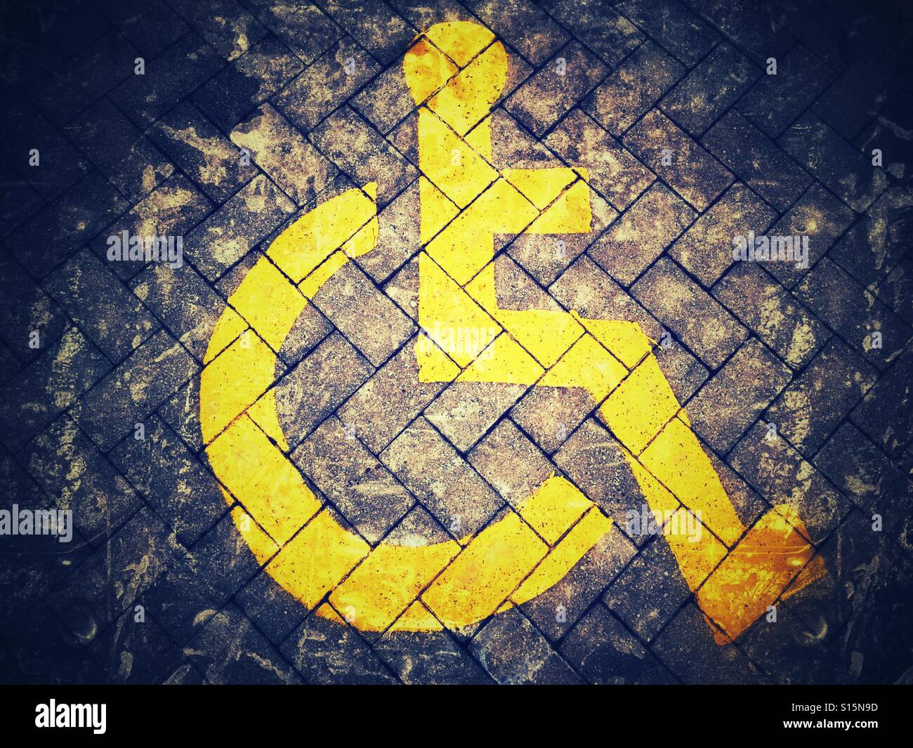 Bright yellow wheelchair symbol painted on dark background Stock Photo