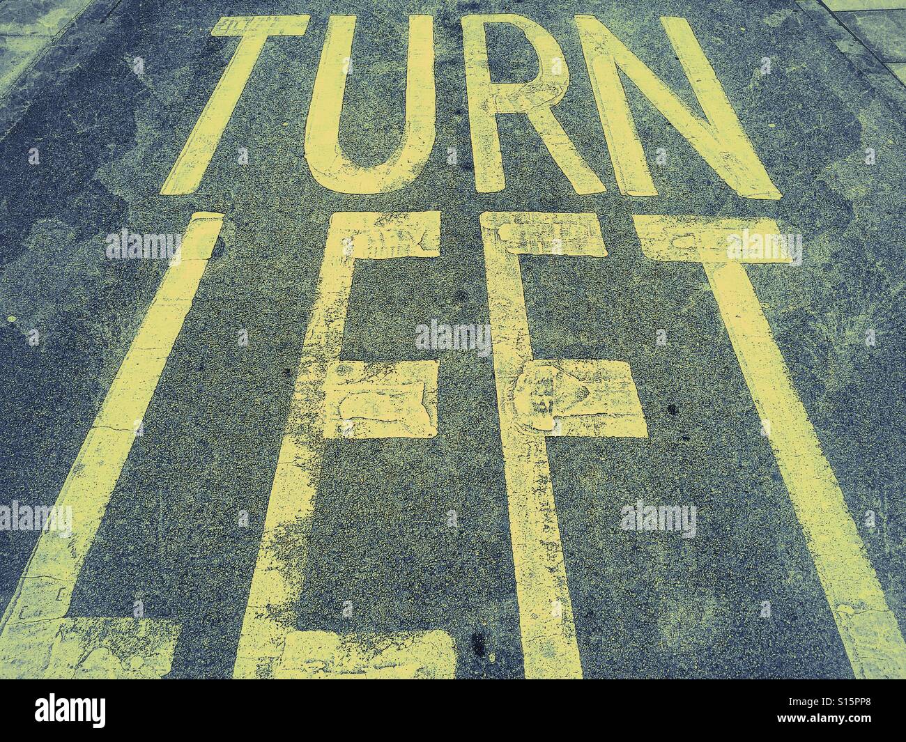 'TURN LEFT' Words painted onto a Tarmac road. Instructions for travellers to turn left at the road junction ahead, as they are joining a one way street. Photo Credit - © COLIN HOSKINS. - Smartphone Captured Stock Image