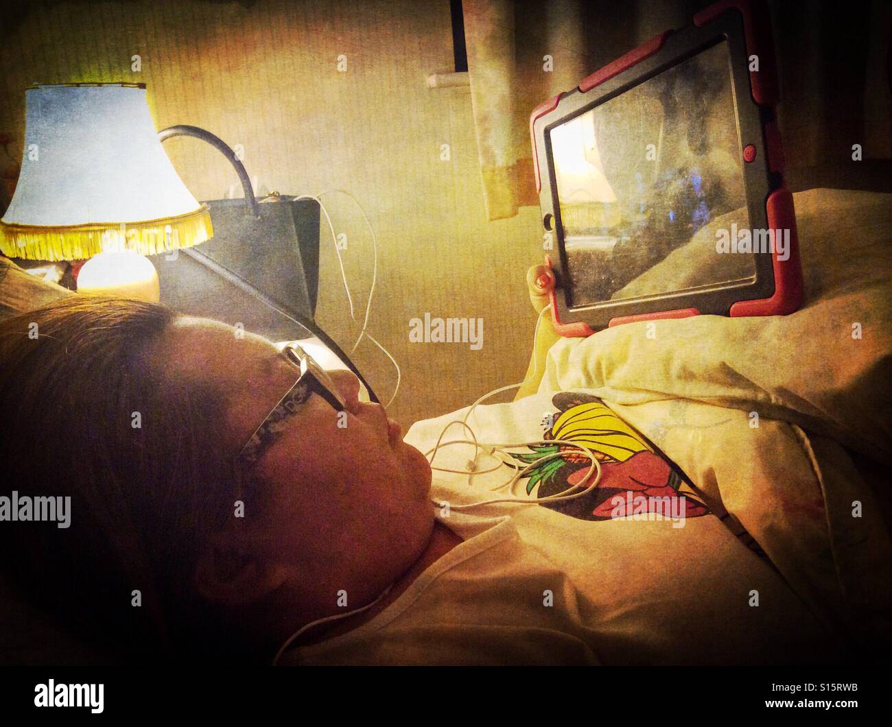 A lady watches a television program on a tablet in bed. - Smartphone Captured Stock Image