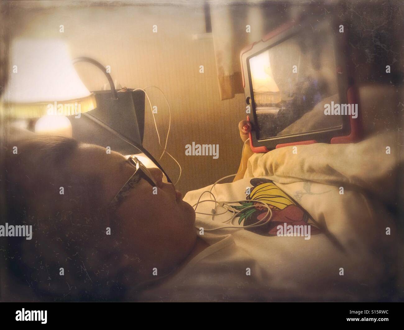 A lady watches a television program on a tablet in bed. - Smartphone Captured Stock Image