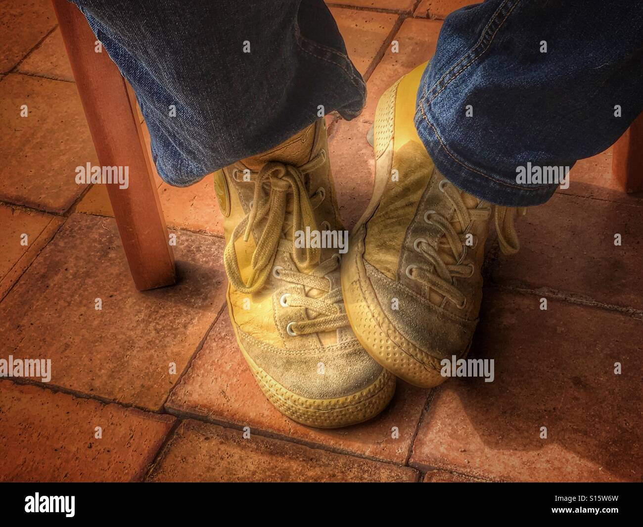 Person with yellow leather sneakers and jeans, sitting on a chair, detail - Smartphone Captured Stock Image
