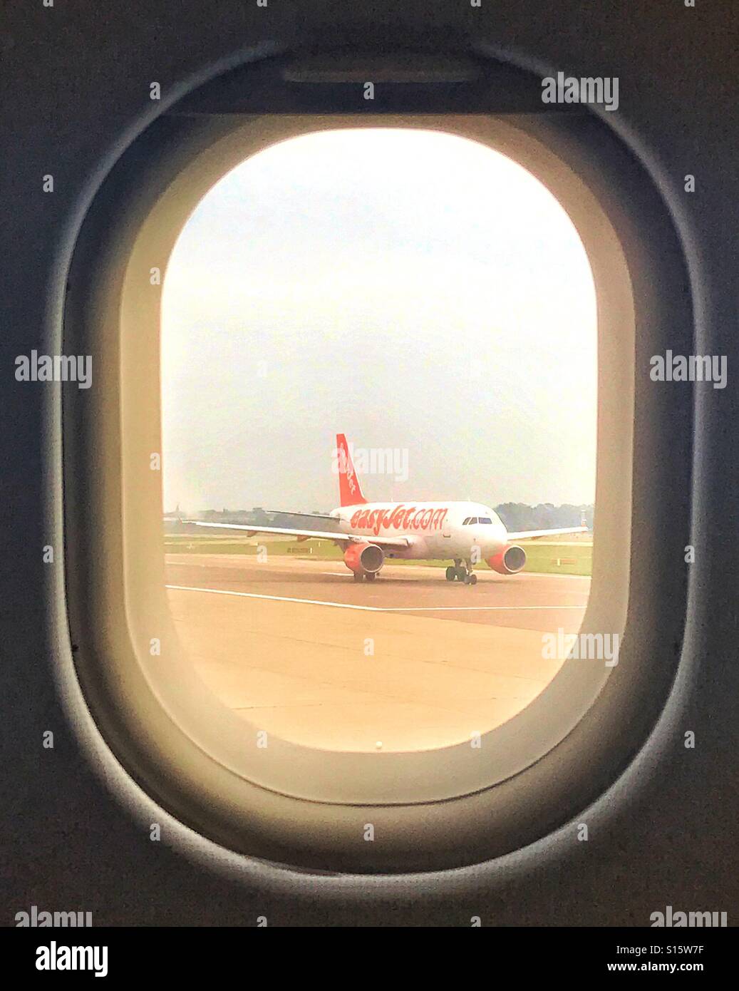 easyJet aircraft on runway awaiting takeoff , viewed through cabin window of another easyJet aircraft - Smartphone Captured Stock Image