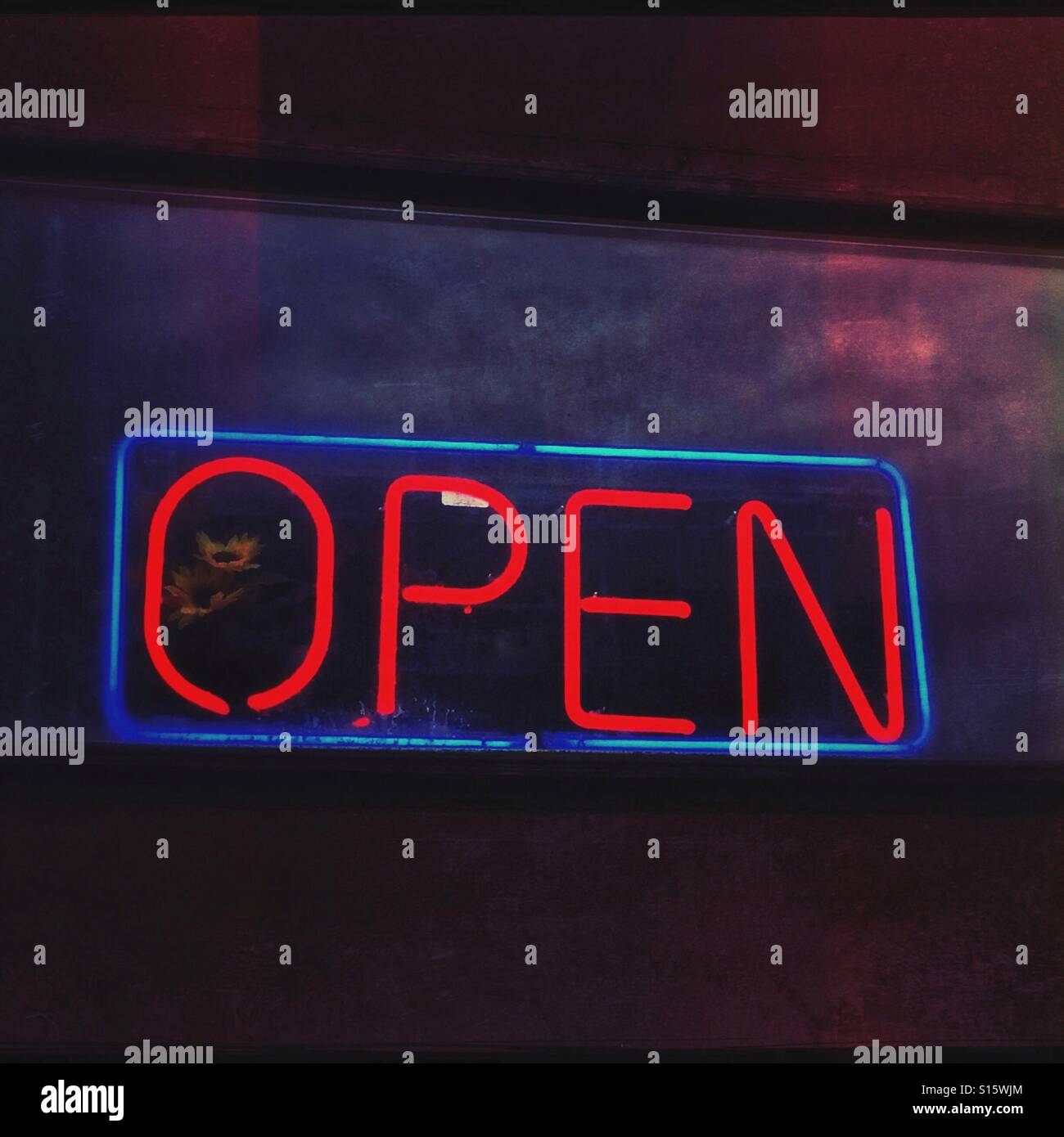 A glowing red neon open sign beckons from a window in the evening. Stock Photo