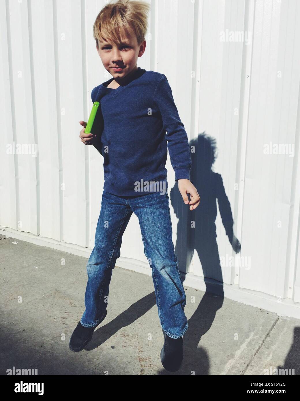 A boy holding a tablet under his arm casts a shadow on a metal-clad wall. - Smartphone Captured Stock Image