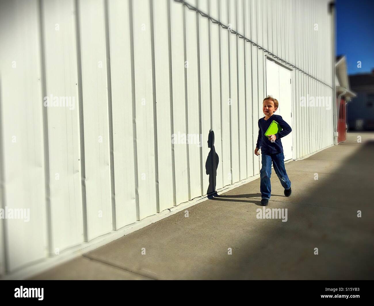 A boy with his tablet under his arm skips beside a commercial building. - Smartphone Captured Stock Image