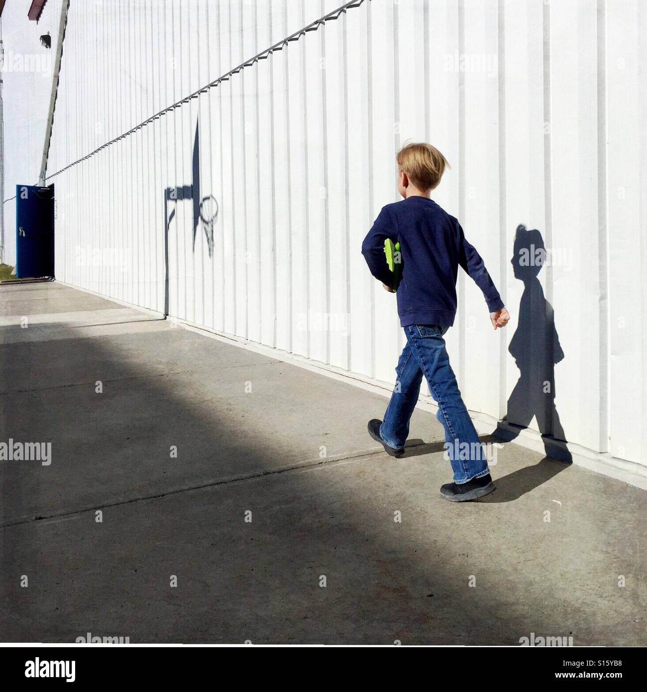 A boy with his tablet under his arm walks briskly alongside a commercial building toward an open door. - Smartphone Captured Stock Image