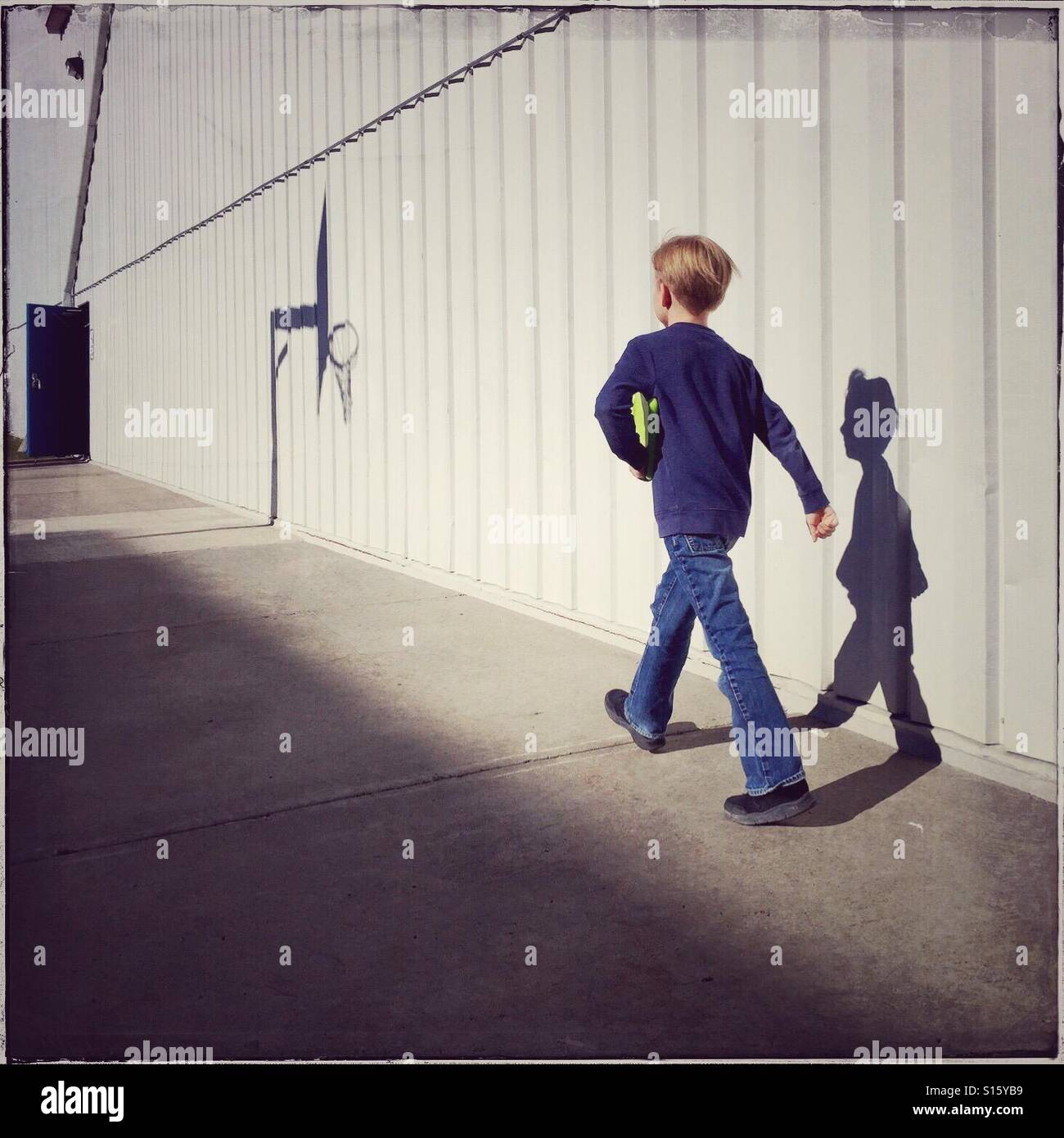 A boy with his tablet under his arm walks briskly alongside a commercial building toward an open door. - Smartphone Captured Stock Image