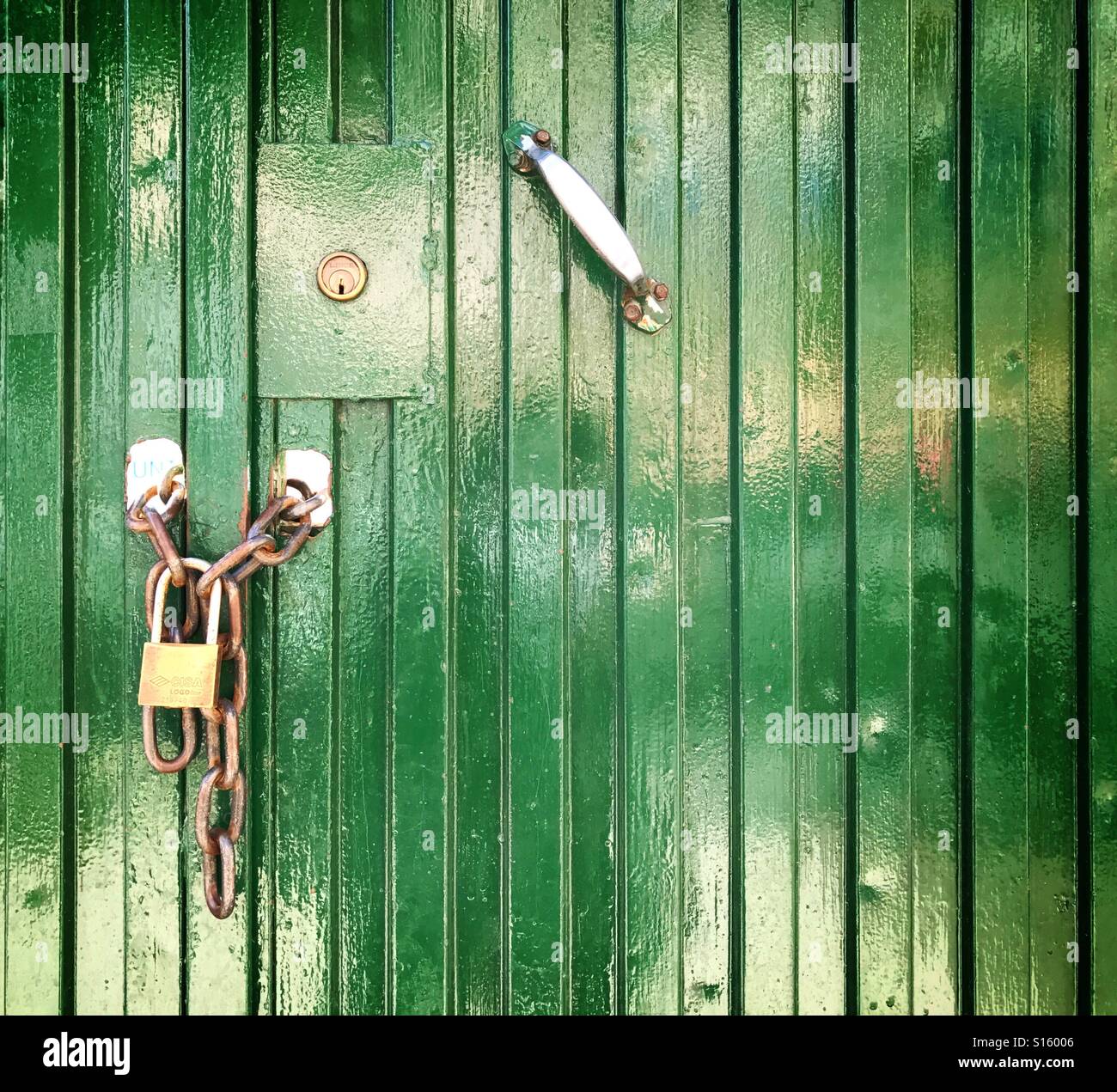 Metal entrance door painted green looked with brass padlock and chain Stock Photo