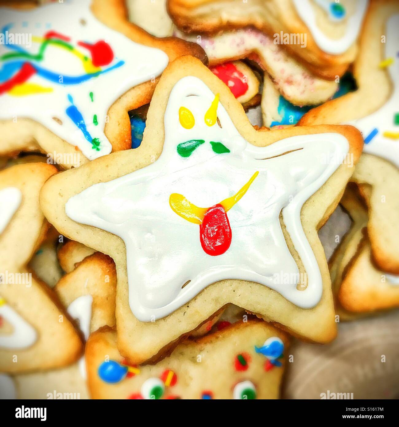 A star-shaped cookie with funny face icing lies atop a pile of cookies. - Smartphone Captured Stock Image