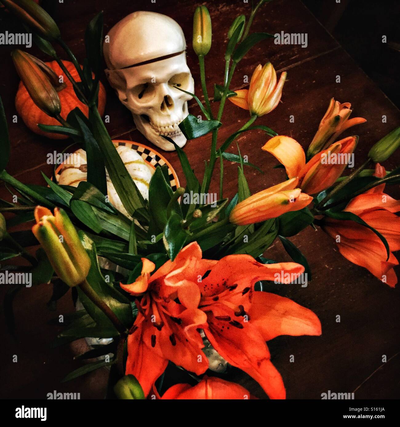A bouquet of orange lilies and a skull decorate a tabletop for Halloween. Stock Photo