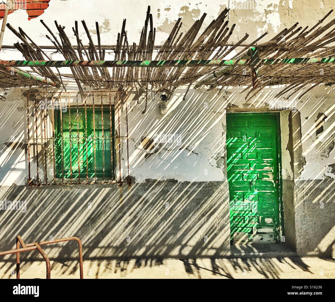 Exterior of dwelling with green door and barred green shuttered window shaded by overhead bamboo canopy - Smartphone Captured Stock Image